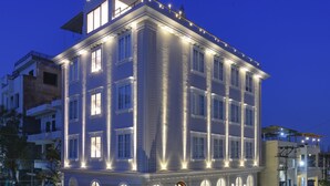 A multi-story building with illuminated windows and a balcony, surrounded by other structures. - Dev Panache (Udaipur)