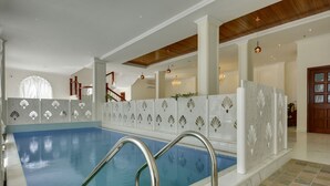 An indoor swimming pool with a blue and white tiled floor, surrounded by a white decorative wall with shell patterns. - Dev Panache (Udaipur)