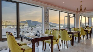 A dining area with large windows, a chandelier, and a view of the cityscape. - Dev Panache (Udaipur)