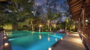 A wooden deck surrounding a clear blue pool with stone lanterns, surrounded by lush greenery and palm trees. - Villa Kapungkur (Jimbaran)