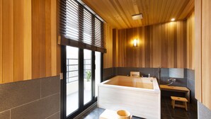 A modern bathroom with a large bathtub, wooden paneling, and a small wooden stool. - Tomonoya Hotel & Ryokan Gyeongju (Gyeongju)