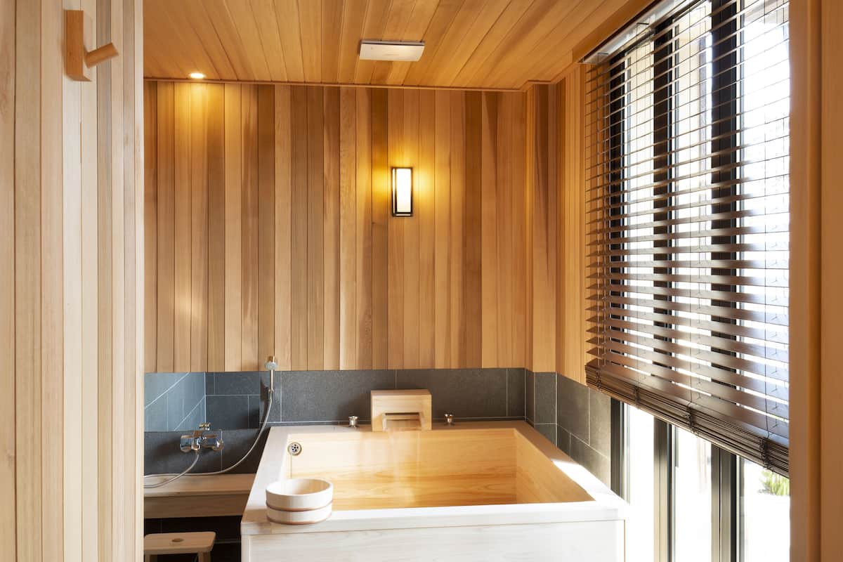 A modern bathroom with a wooden interior, a freestanding bathtub, and a window with blinds.