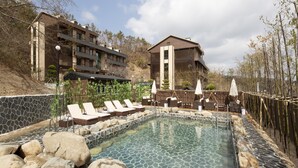 A pool area with lounge chairs, a stone wall, and a building with multiple floors and balconies. - Tomonoya Hotel & Ryokan Gyeongju (Gyeongju)