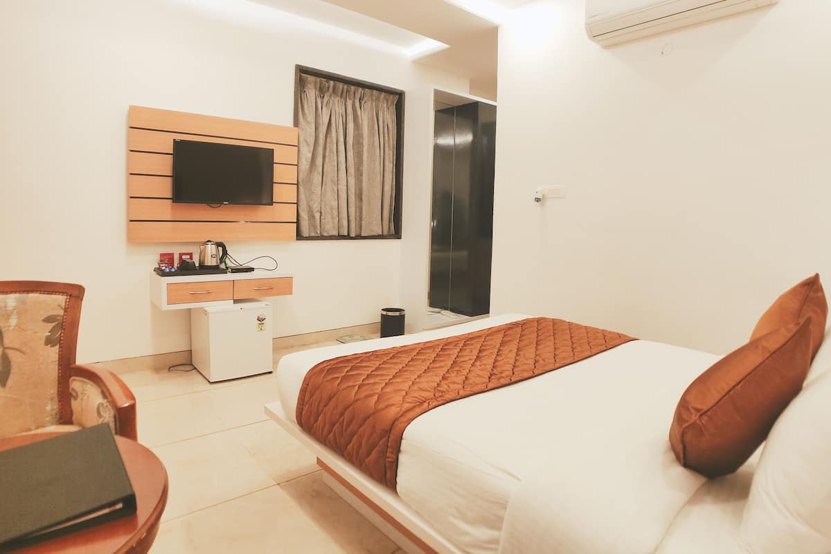 A modern hotel room with a bed, a desk, a television, and an air conditioning unit.