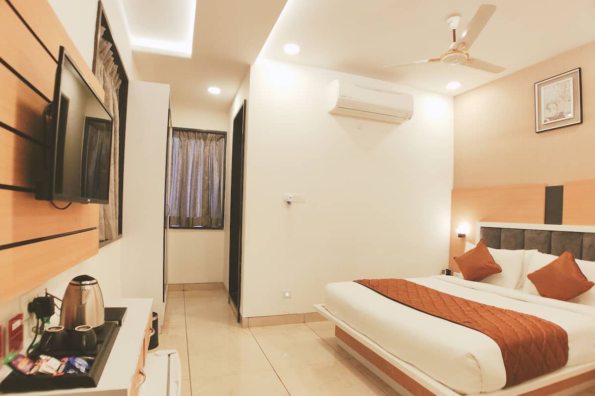 A hotel room with a bed, a TV mounted on the wall, an air conditioner, and a ceiling fan.