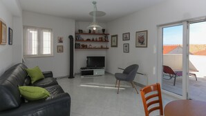 A living room with a black leather sofa, a grey armchair, a TV on a stand, and a glass door leading to an outdoor area. - Apartment Perina (Sutivan)