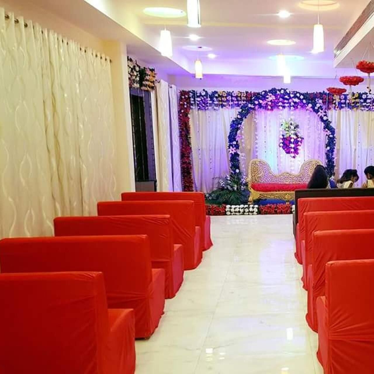 A room with rows of red chairs, a stage with floral decorations, and a white curtain backdrop.