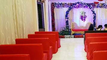A room with rows of red chairs, a stage with floral decorations, and a white curtain backdrop.
