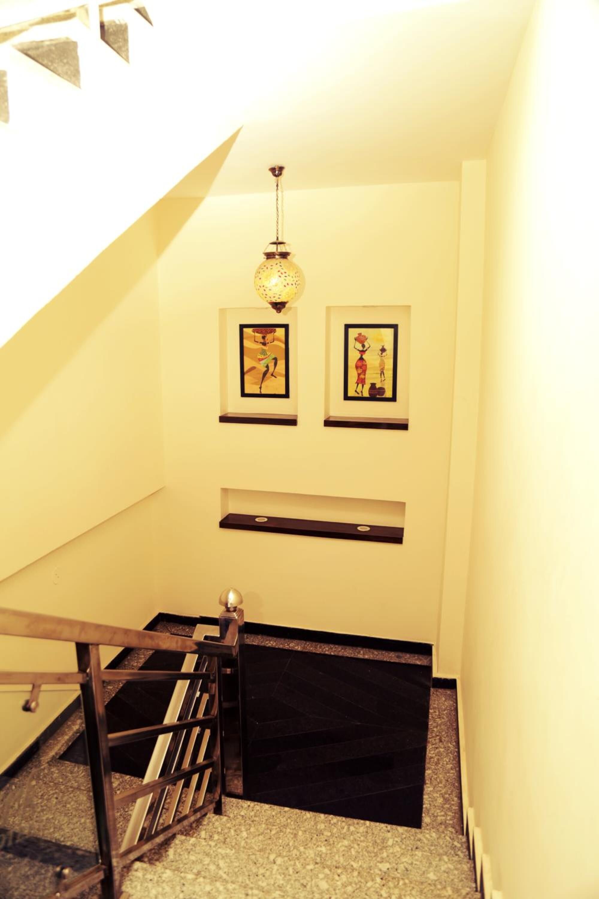 Una escalera con un felpudo negro, barandilla metálica y dos obras de arte enmarcadas en la pared.