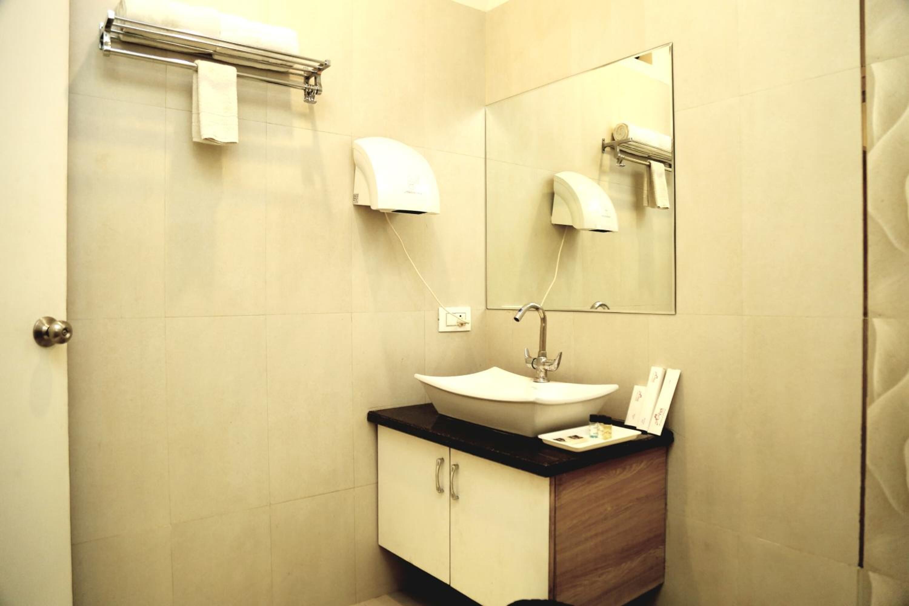 A bathroom with a sink, mirror, towel dispenser, and a wooden vanity.