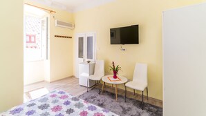 Una habitación pequeña y luminosa con una cama, dos sillas, una mesita, un televisor y una ventana.