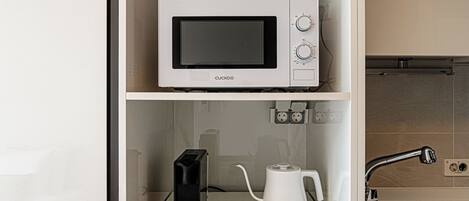A kitchenette with a microwave, coffee maker, and kettle on a white countertop.