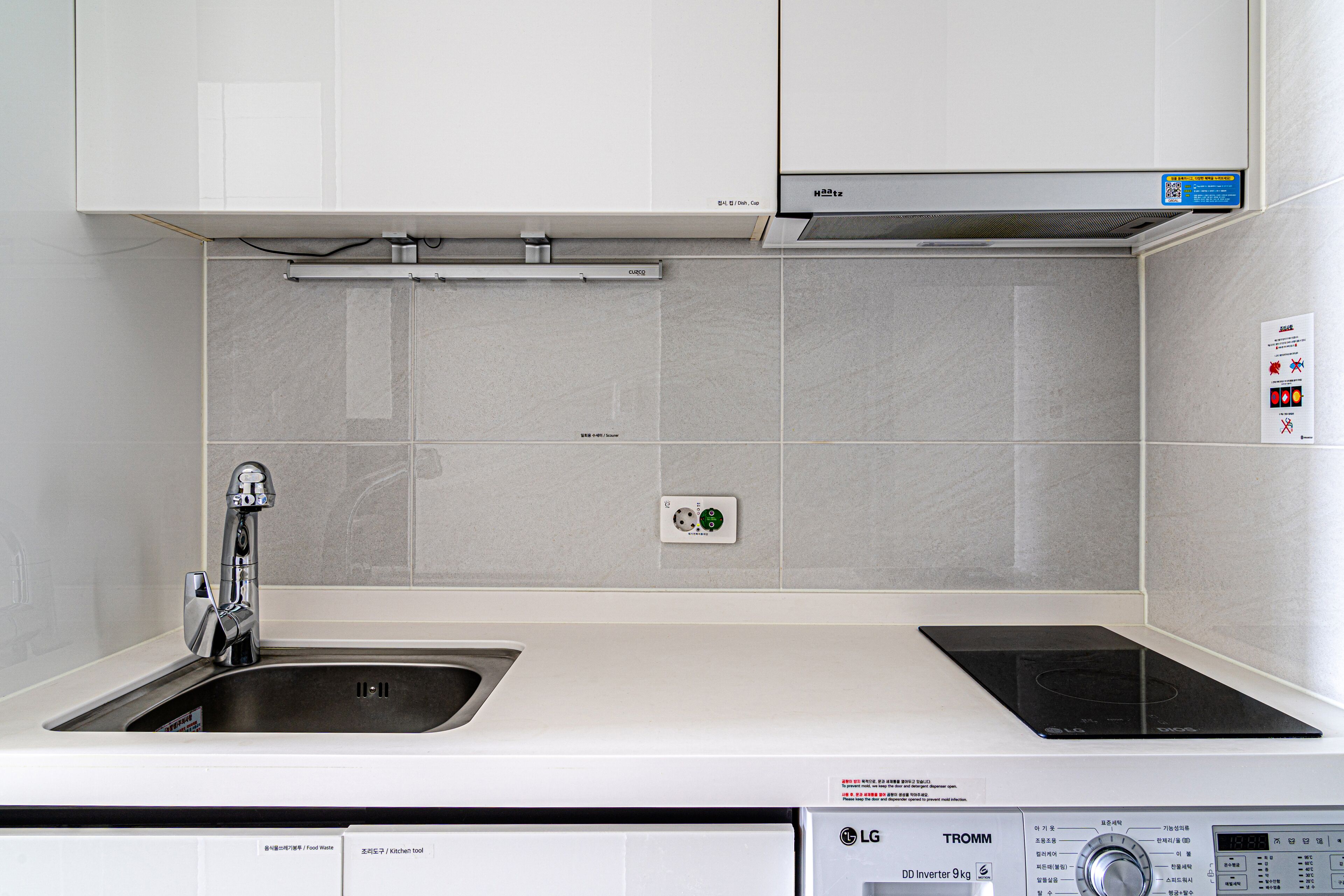 A modern kitchen with a built-in dishwasher, a stainless steel sink, and a black induction cooktop.