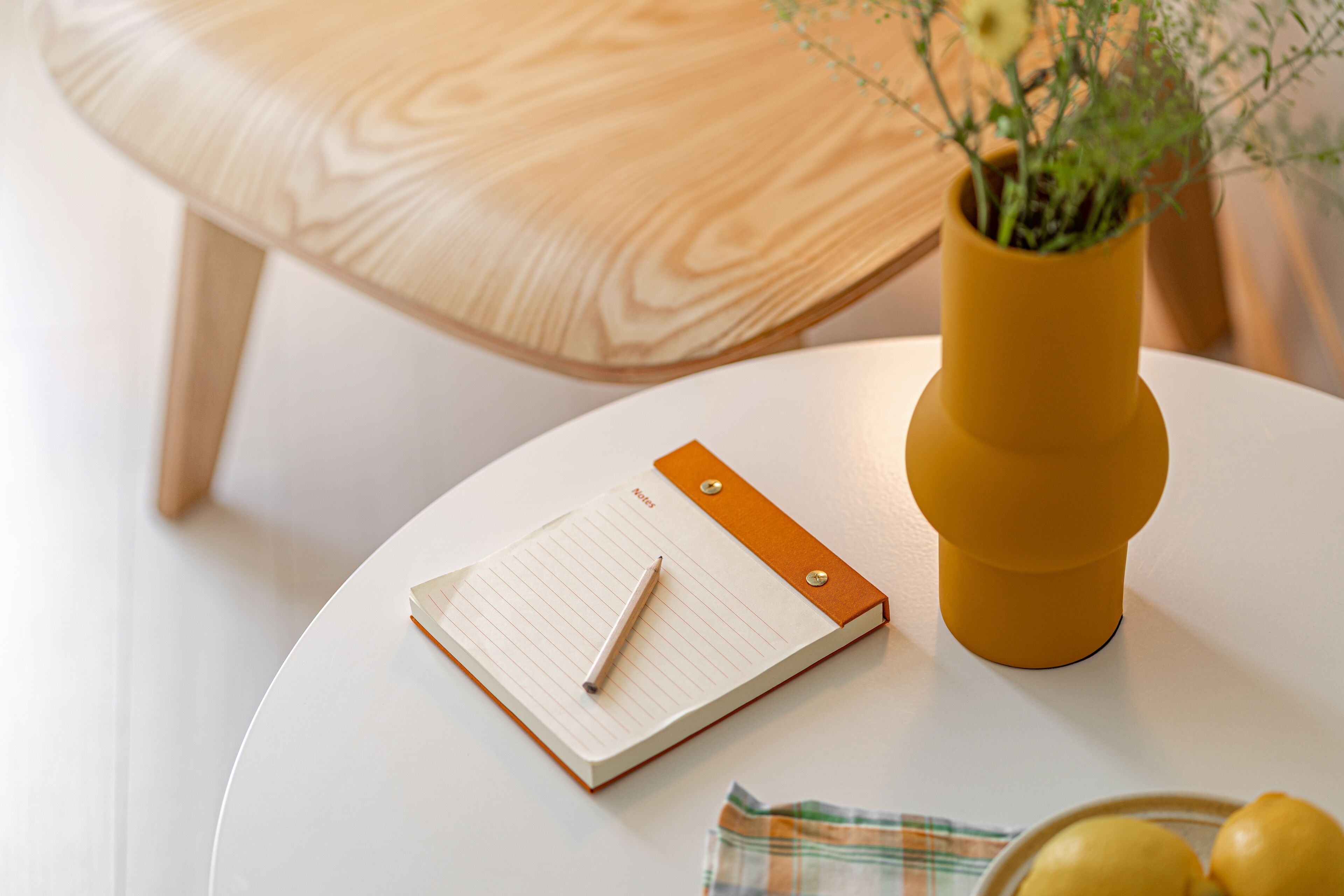 A round white table with a notepad, pen, and a yellow vase with a plant.