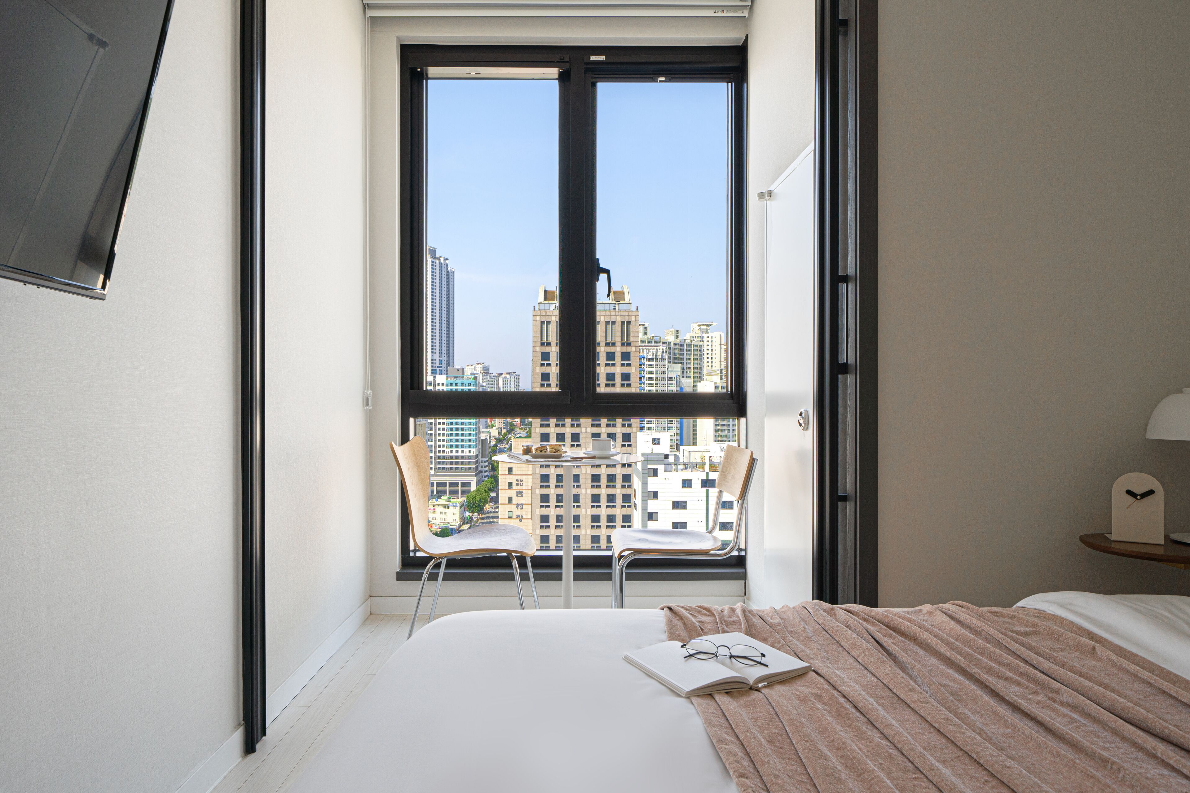 Una habitación de hotel con un ventanal grande, una cama, dos sillas y una mesita.