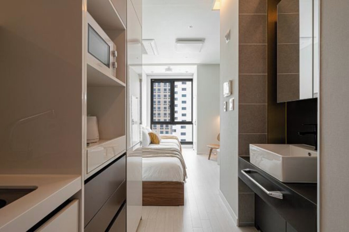 A modern hotel room with a bed, built-in wardrobe, and a bathroom with a large mirror and sink.