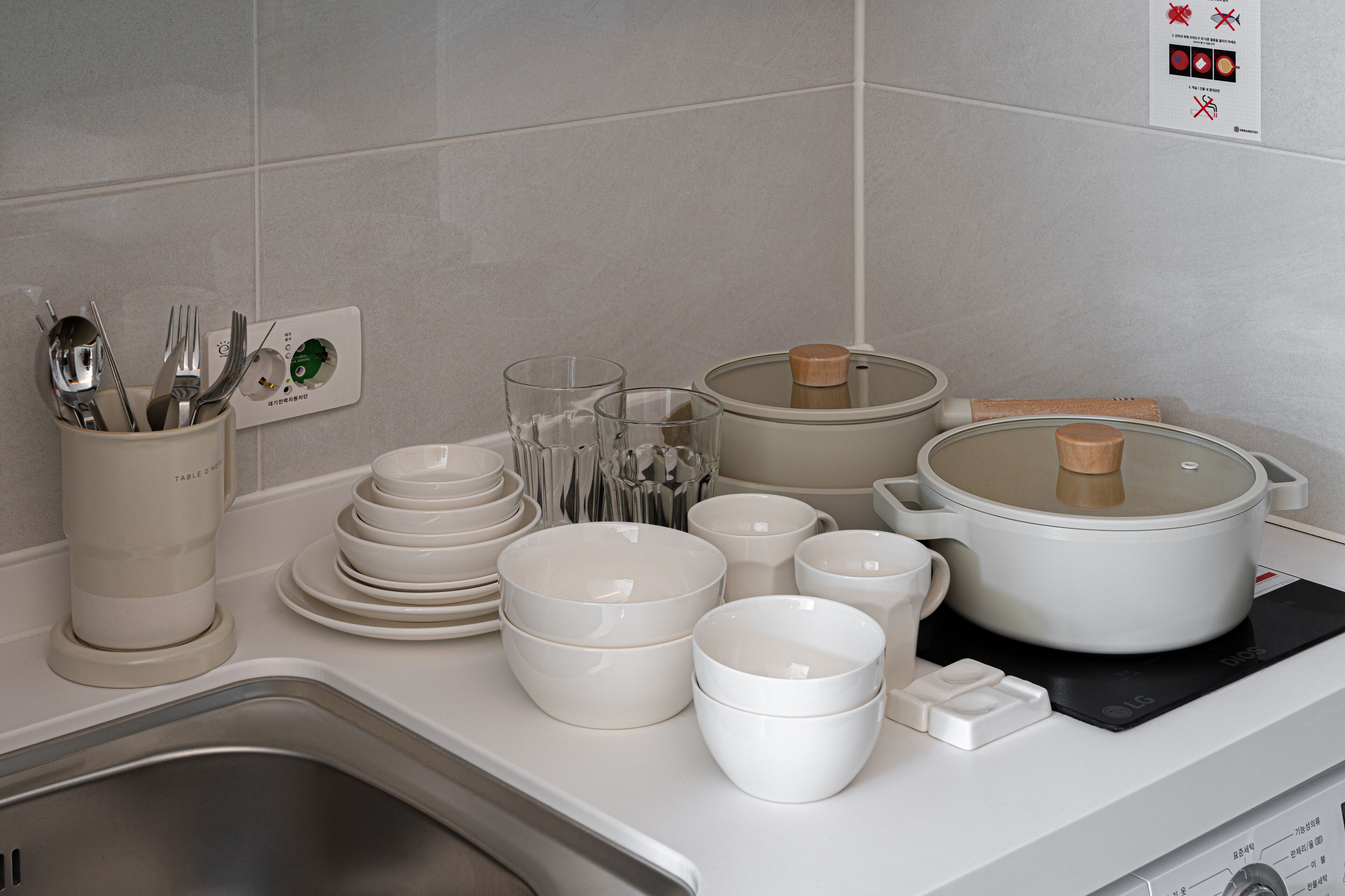 A kitchen counter with various white dishes, a rice cooker, and a utensil holder.