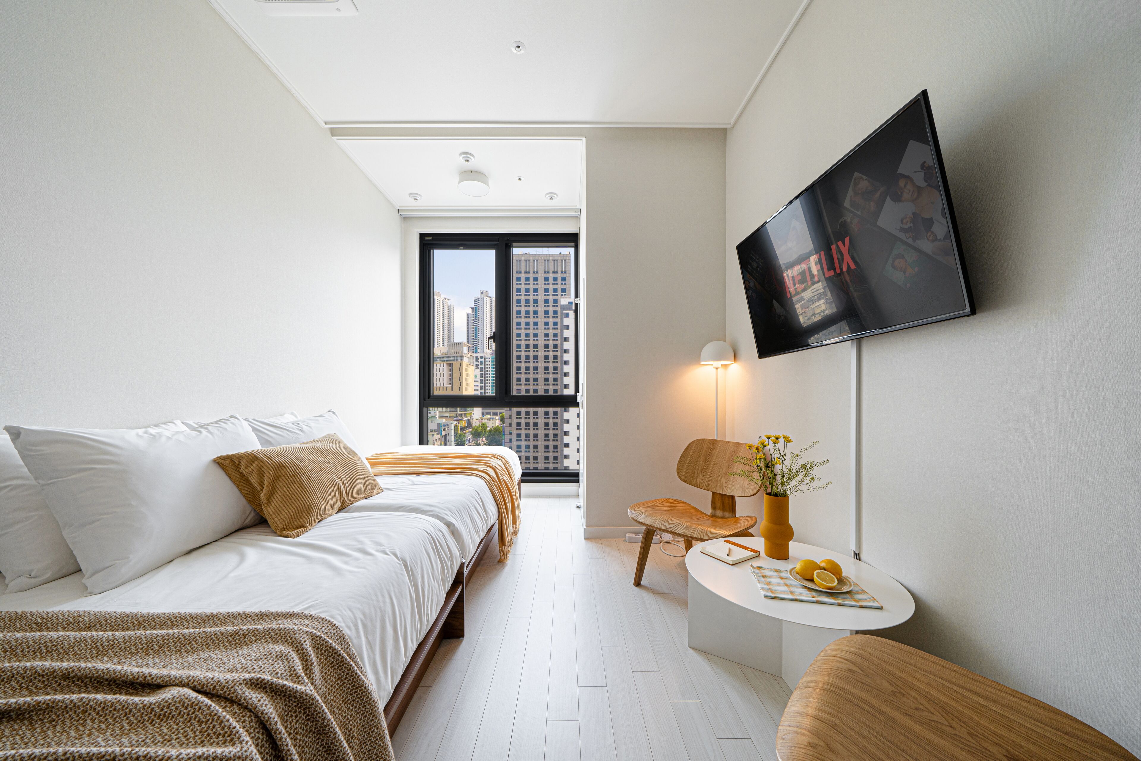 Habitación de hotel moderna con cama, una mesita de noche con un florero y un televisor montado en la pared.