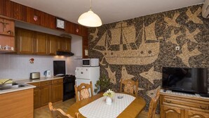 A kitchen with wooden cabinets, a microwave, a stove, and a dining area with a table and chairs. - Apartment Horizont (Dubrovnik)