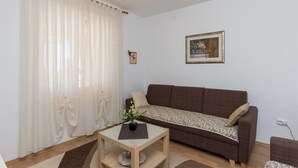 A living room with a brown sofa, a small table with a plant, and a framed picture on the wall. - Apartment Horizont (Dubrovnik)