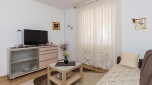 A modern living room with a flat-screen TV, a wooden cabinet, a small table with a plant, a sofa, and a patterned rug. - Apartment Horizont (Dubrovnik)