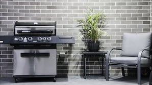 A barbecue grill, a potted plant, and a chair against a brick wall. - Quiet relaxing Location,2 Bedroom 2 Bathroom Guesthouse.Walking distance to CBD. (Mudgee)