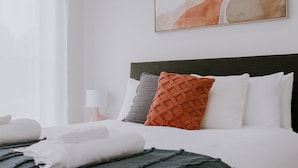 A neatly made bed with white and gray linens, a dark gray throw blanket, and a variety of pillows including a red one. A large abstract painting hangs above the bed. - Quiet relaxing Location,2 Bedroom 2 Bathroom Guesthouse.Walking distance to CBD. (Mudgee)