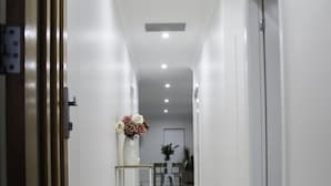 A clean, modern hallway with a shiny tiled floor, a vase of flowers on a small table, and a door on the right. - Quiet relaxing Location,2 Bedroom 2 Bathroom Guesthouse.Walking distance to CBD. (Mudgee)