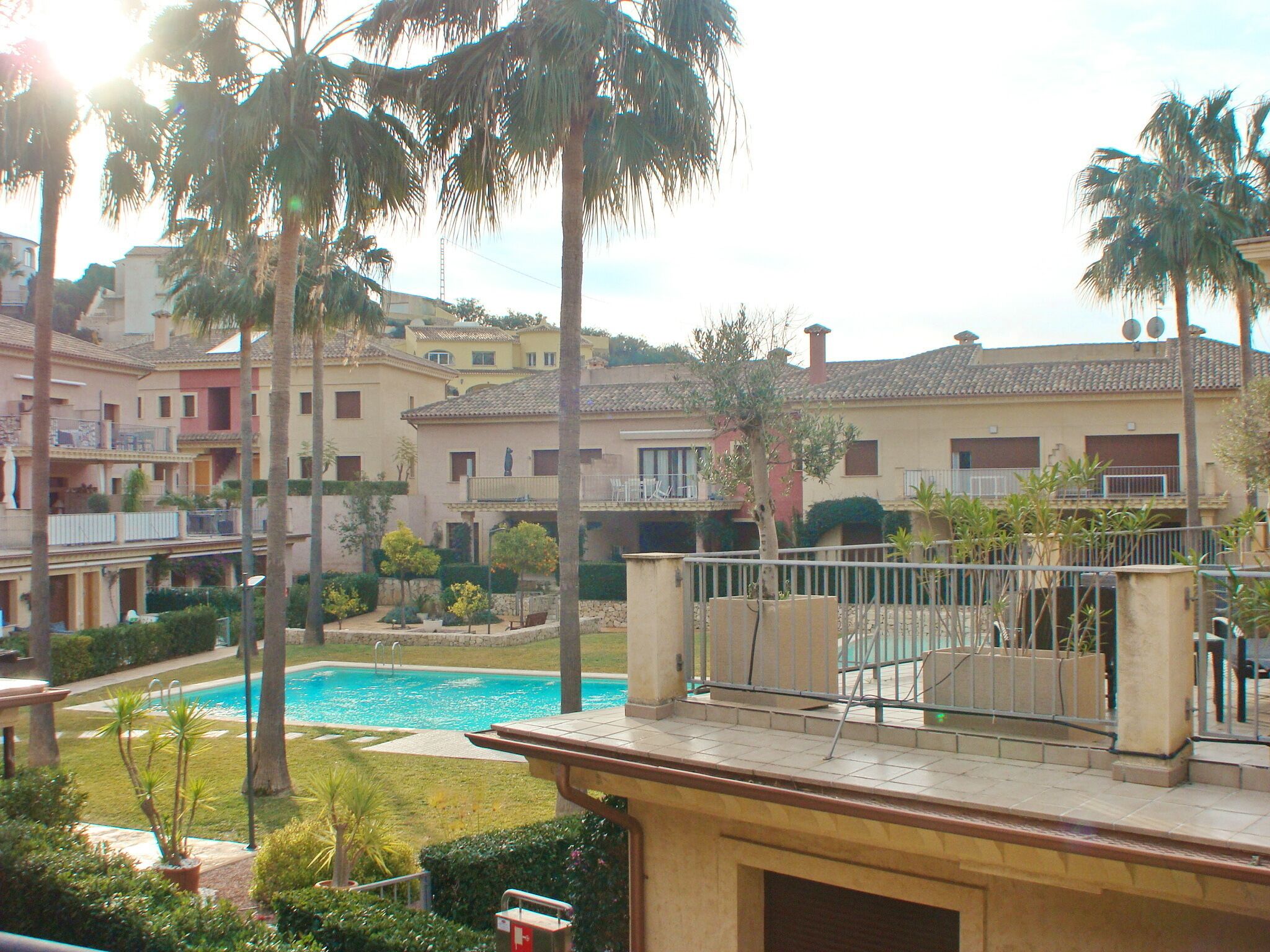 Zona residencial con piscina rodeada de palmeras y casas con balcones.