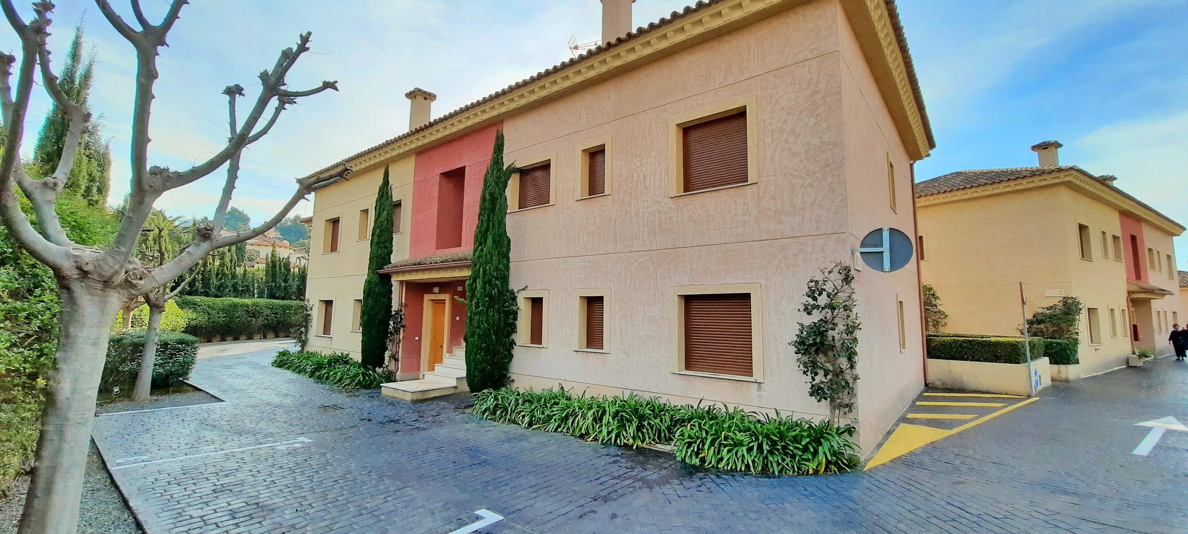 A two-story building with a red door, multiple windows, and a paved courtyard.