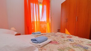 Makuuhuoneessa on sänky, puinen vaatekaappi ja ikkuna, jossa on oranssit verhot.