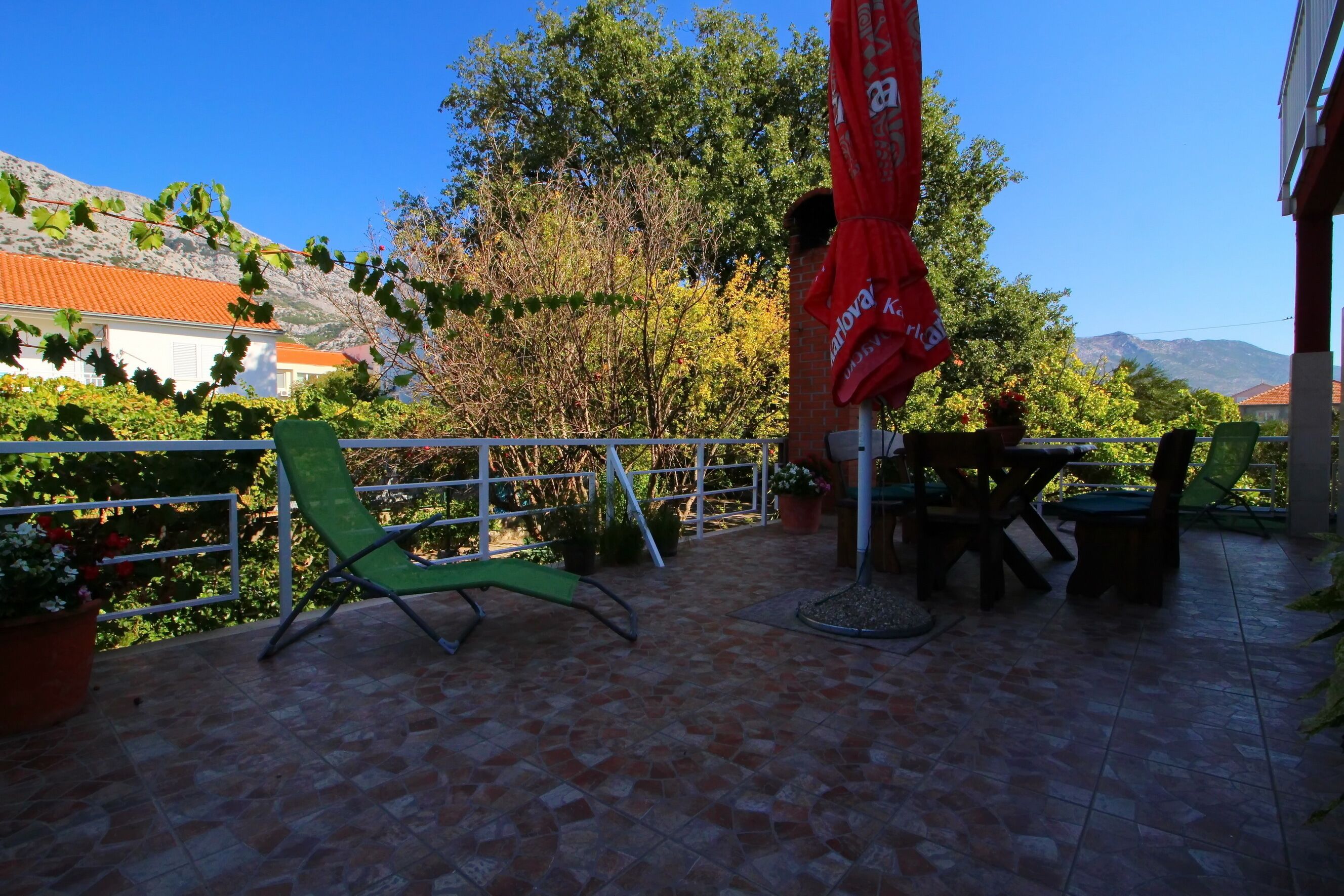 A patio with a green chair, a table with chairs, and a red umbrella.