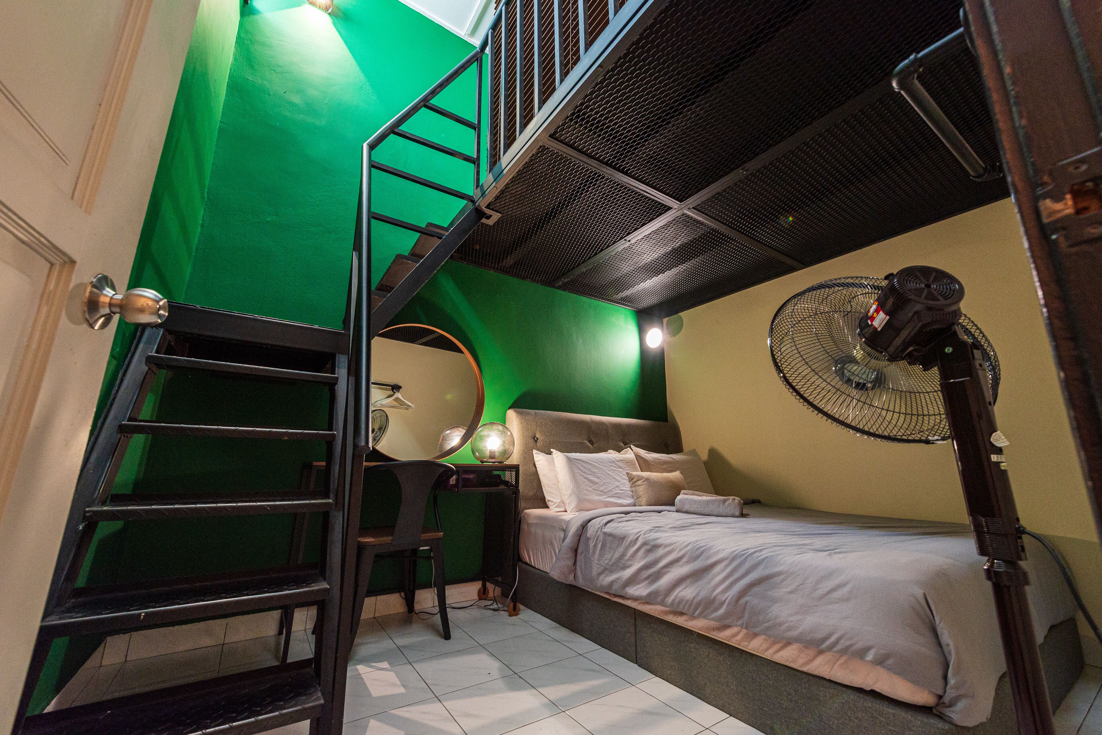 Un dormitorio con cama, escritorio, silla, pared verde, escalera y ventilador de techo.