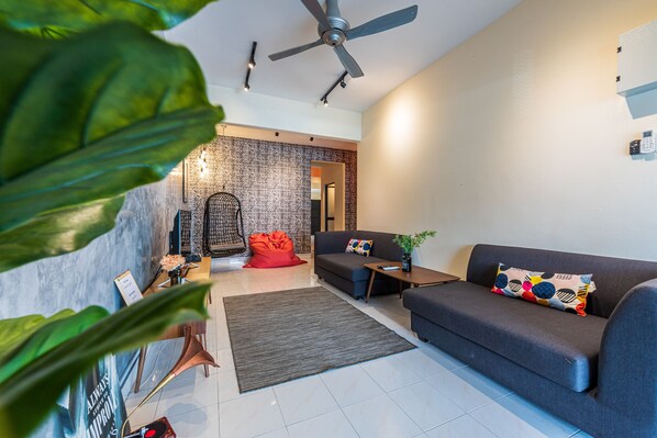 A modern living room with a grey sofa, a red bean bag, a small table with a plant, and a ceiling fan.