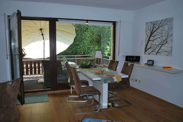 A dining area with a table, chairs, and a view of greenery through a glass door. - Vacation apartment AltesSalzwerk (Bad Harzburg)