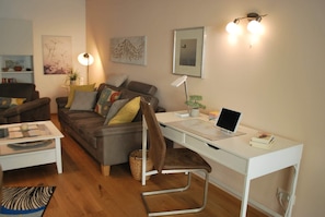 A living room with a sofa, a desk with a laptop, and a lamp. - Vacation apartment AltesSalzwerk (Bad Harzburg)