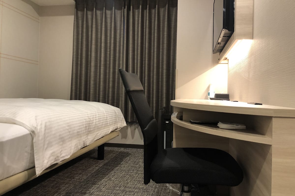 Une chambre d’hôtel avec un lit, un bureau et une chaise, une télévision et un rideau.