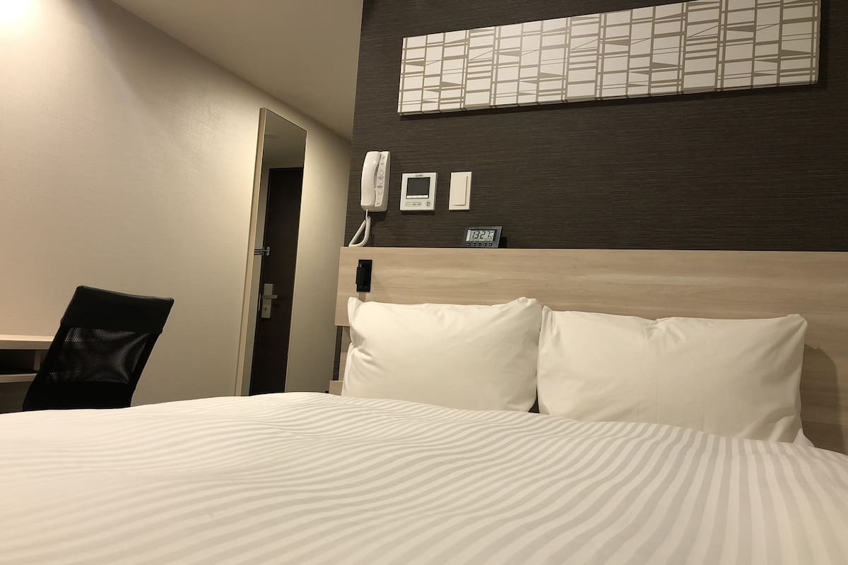 Une chambre d’hôtel équipée d’un lit, d’un bureau, d’une chaise, d’un téléphone et d’une horloge murale.