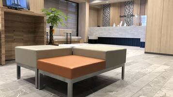 A modern hotel lobby with a reception desk, seating area, and a large window.