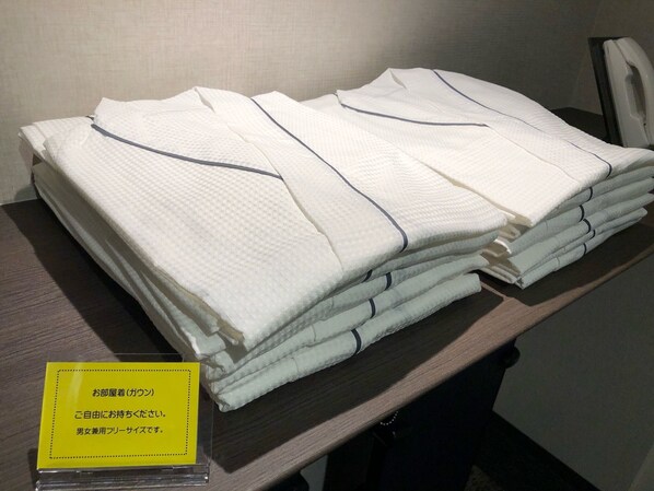 A stack of neatly folded white towels with dark trim on a wooden surface, accompanied by a yellow sign with Japanese text. - Smile Hotel Osaka Nakanoshima (Osaka)