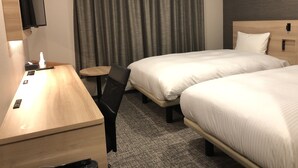 A hotel room with two beds, a desk with a chair, a small table, a TV mounted on the wall, and a window with curtains.