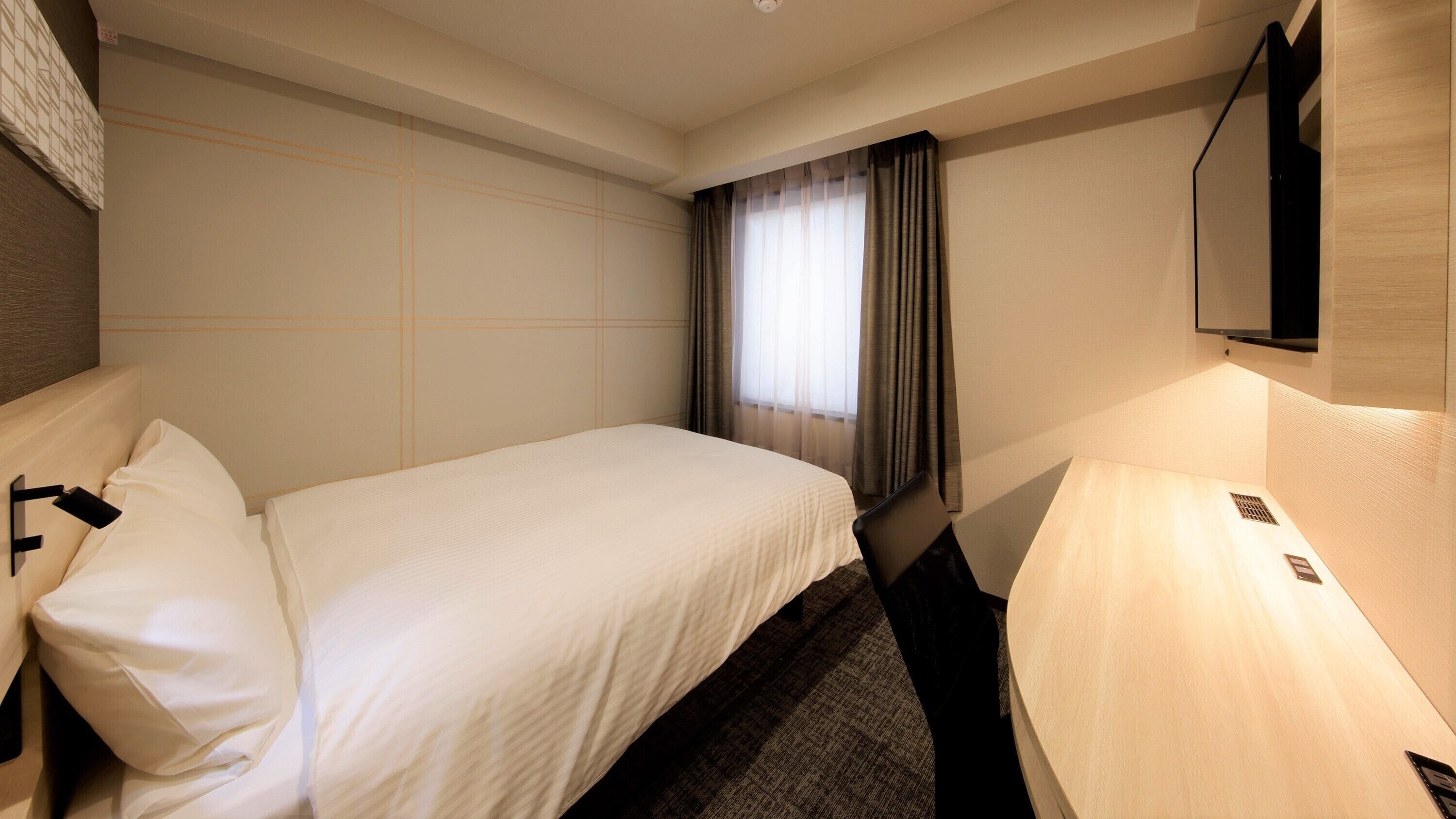 A hotel room with a bed, a desk, a chair, a TV, and a window with curtains.