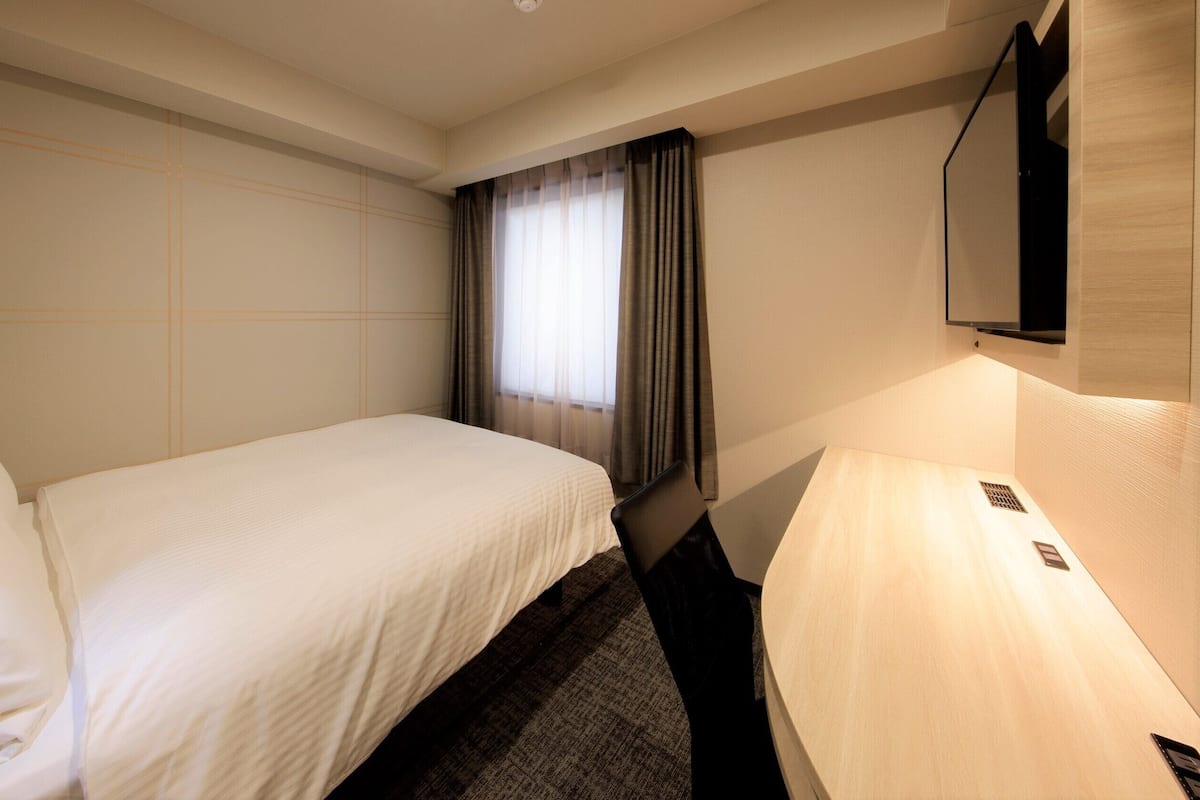 Une chambre d’hôtel équipée d’un lit, d’un bureau, d’une chaise, d’une télévision et d’une fenêtre avec des rideaux.