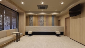 A modern hotel reception area with a counter, seating, and a TV mounted on the wall.