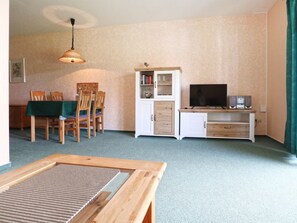 Ein Wohnzimmer mit Esstisch, Stühlen, Fernseher, Lautsprechern und einem Schrank.