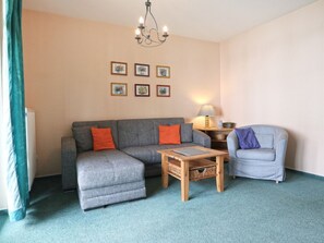 Ein Wohnzimmer mit grauem Sofa, blauem Sessel, Couchtisch aus Holz und einer Kristallleuchtre.