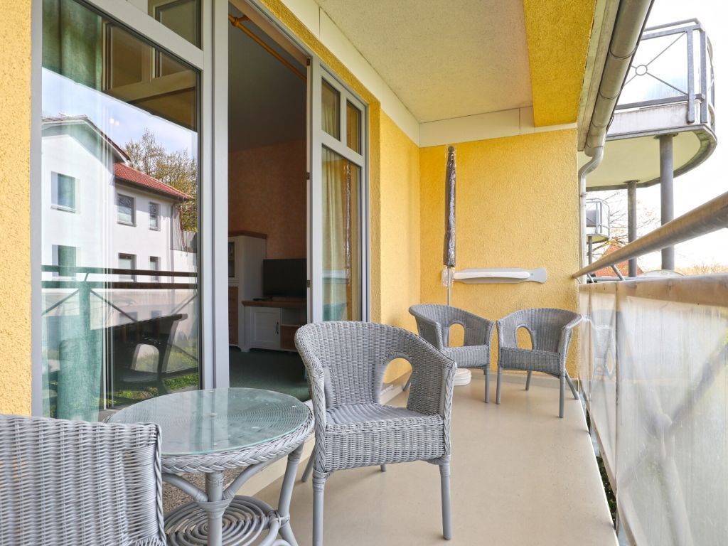 An outdoor balcony with wicker furniture and a glass table, overlooking a residential area.