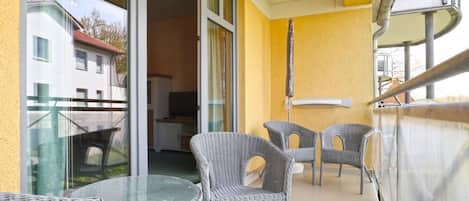 Ein Balkon im Freien mit Korbmöbeln und einem Glastisch mit Blick auf eine Wohngegend.