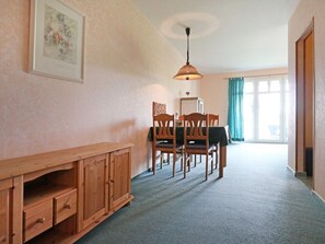 Ein Essbereich mit Holztisch und Stühlen, einer Kommode mit Schubladen, einer Hängeleuchte und einem großen Fenster mit Vorhängen.