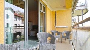 An outdoor balcony with wicker furniture and a glass table, overlooking a residential area. - Minervapark Whg. Mi13 (Ostseebad Boltenhagen)